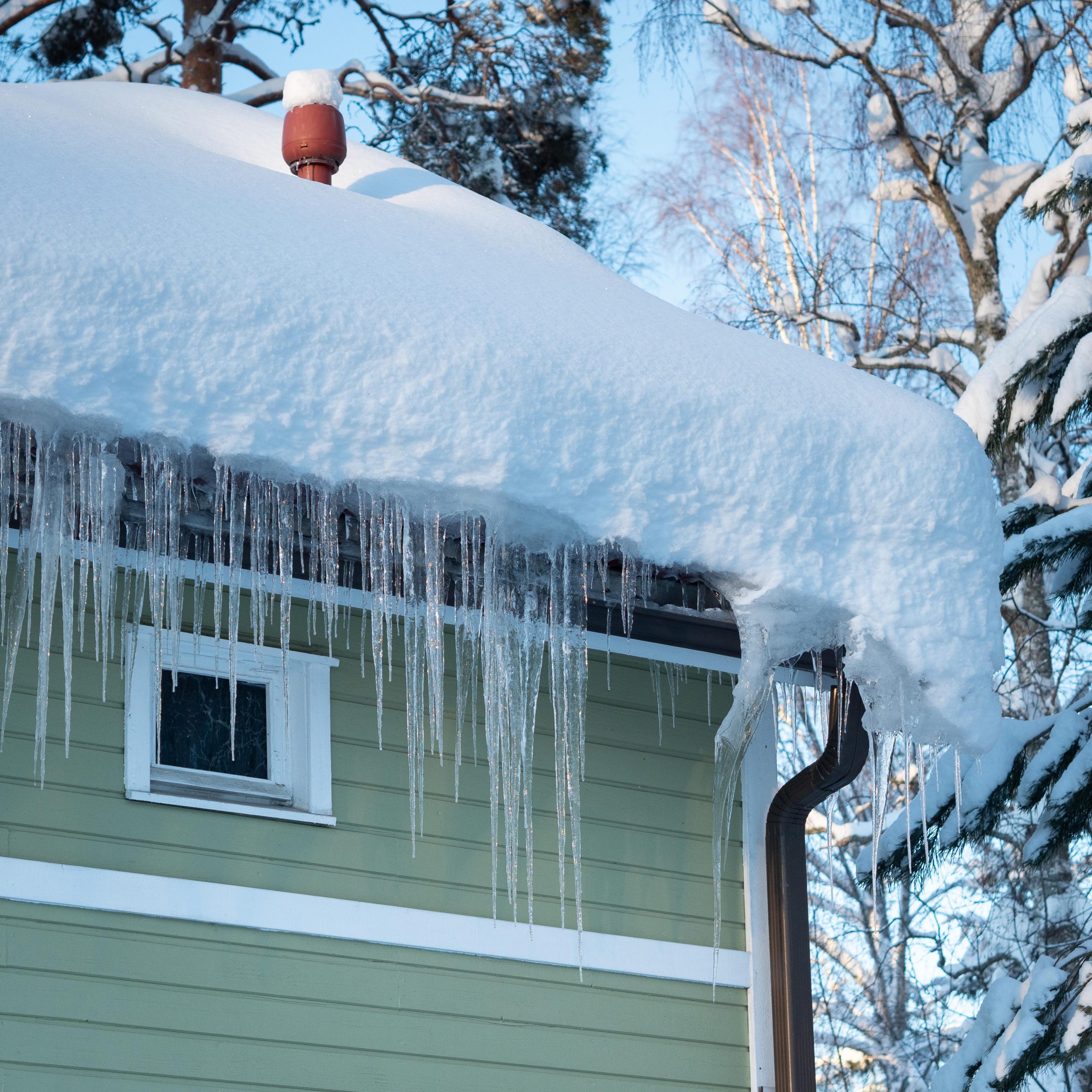 Jääpuikkoja roikkumassa vihreän puutalon katon reunalla.