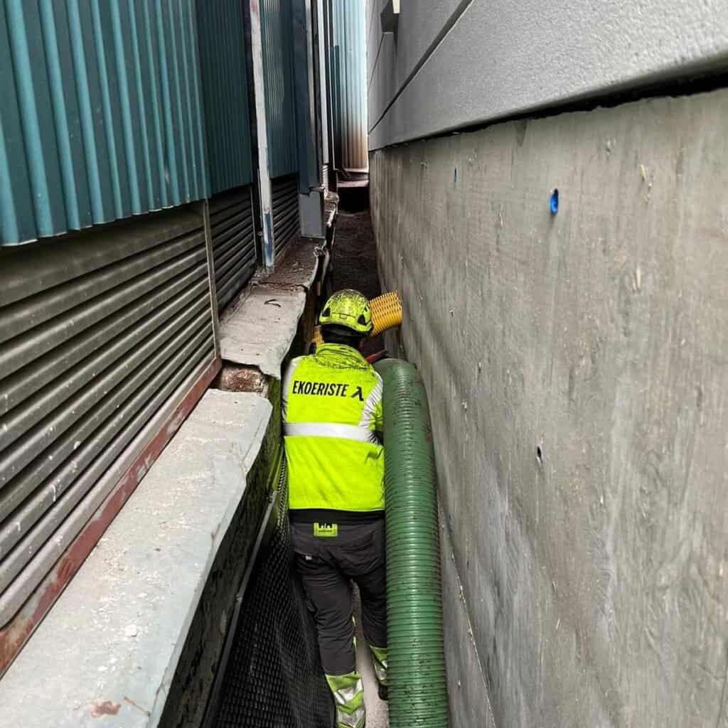 Ekoeristeen asentaja puhaltaa lecasoraa kapeaan kaivantoon